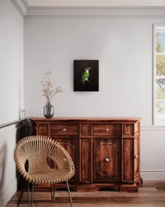 Das Foto zeigt das Gemälde eines Grünspechts, eingefügt in ein Interieur mit einer Holzkommode und einem Korbstuhl.