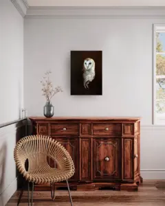 Das Foto zeigt das Gemälde einer Schleiereule, eingefügt in ein Interieur mit einer Holzkommode und einem Korbstuhl.